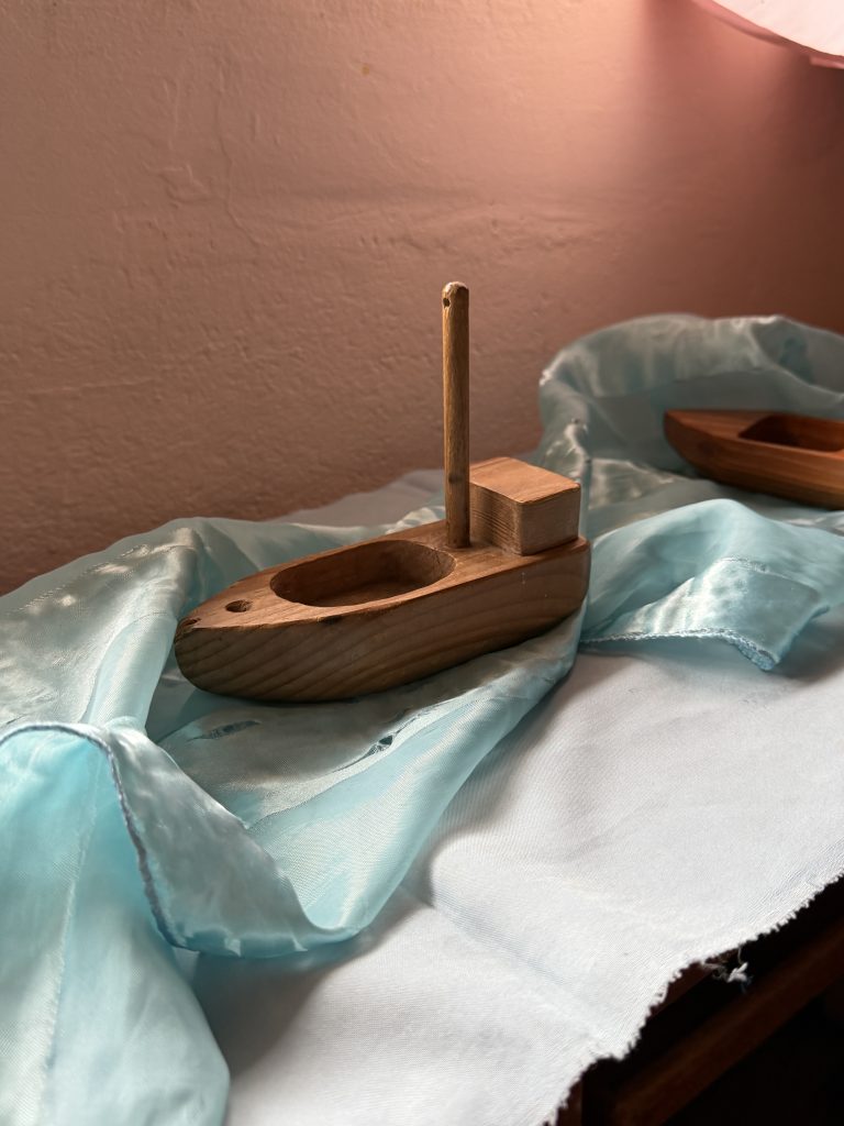 A simple wooden toy boat resting on blue silk