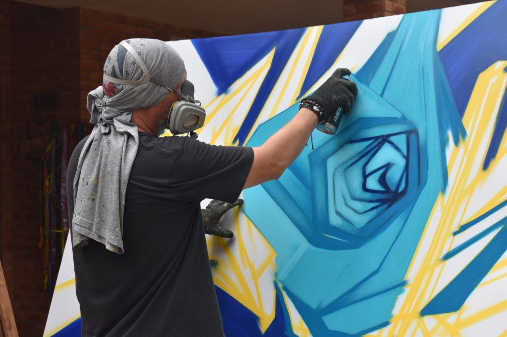 A graffiti artist spray painting a large blue and yellow mural at the Roseway Arts Festival