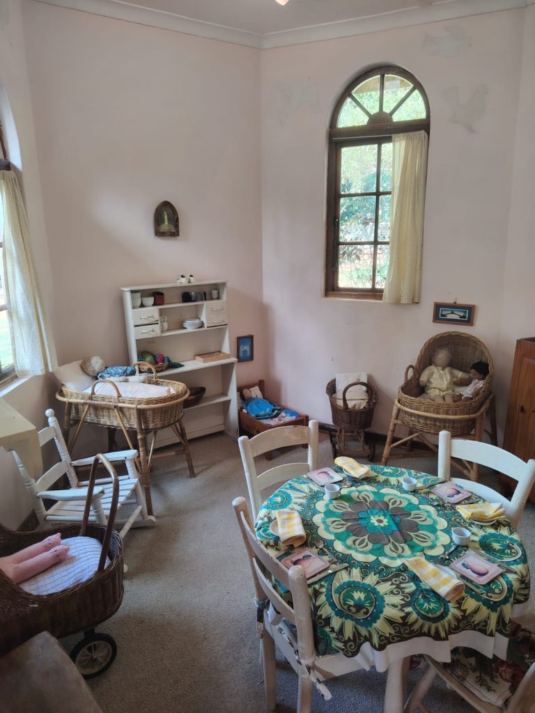 A home-like early childhood playroom with a dolls corner and a table set for snack time