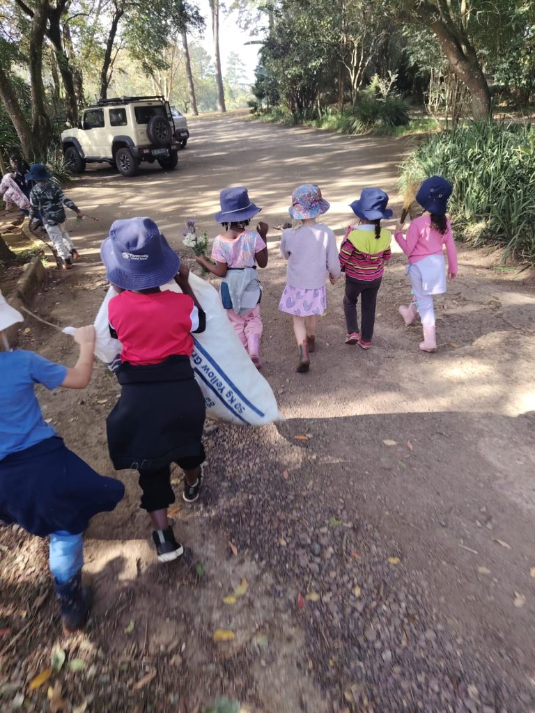 Kindergarten children in sunhats walking along a tree-lined farm road