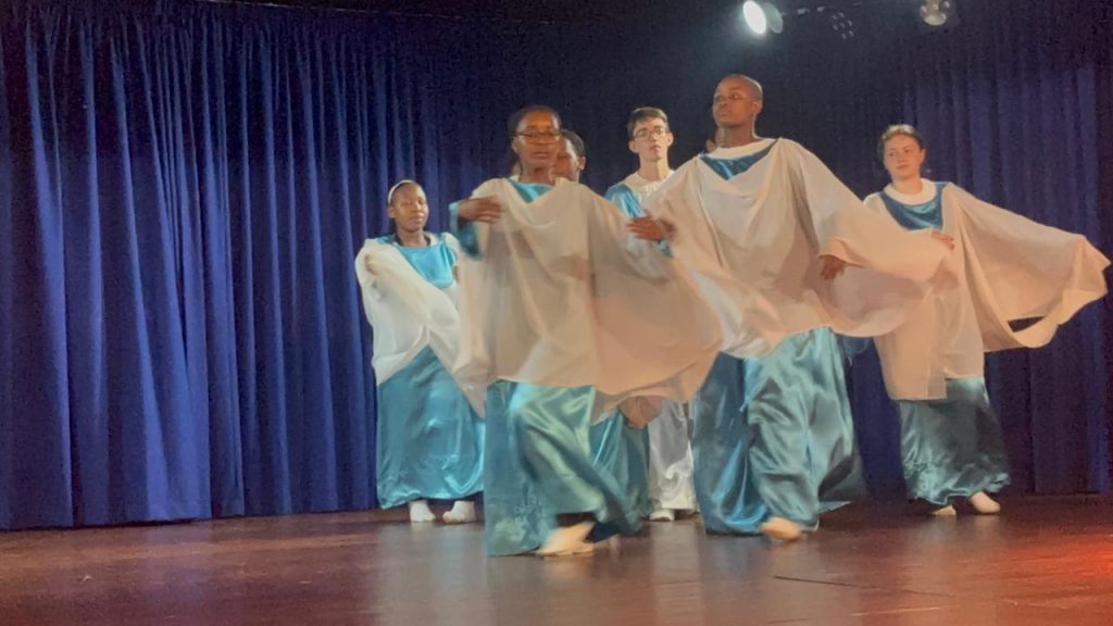 Class 12 students in flowing costumes performing eurythmy on stage